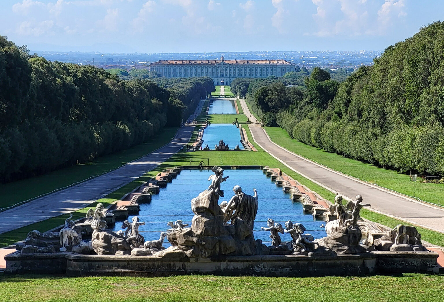 the Royal Palace of Caserta, a grand 18th-century palace in Italy, featuring a Late Baroque and early Neoclassical architectural style, with a large courtyard and ornate fountains, inspired by the Palace of Versailles.