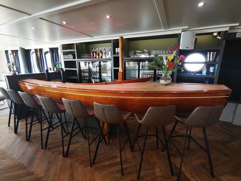 The bar on the Magnifique IV, a luxury river barge, offers a sophisticated setting with large panoramic windows and a lounge area.