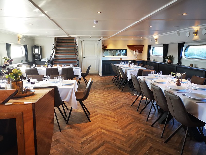 The elegant dining room of the Magnifique IV, located on the lower deck, offers breakfast and three-course dinners prepared by skilled chefs, visible through a glass wall.