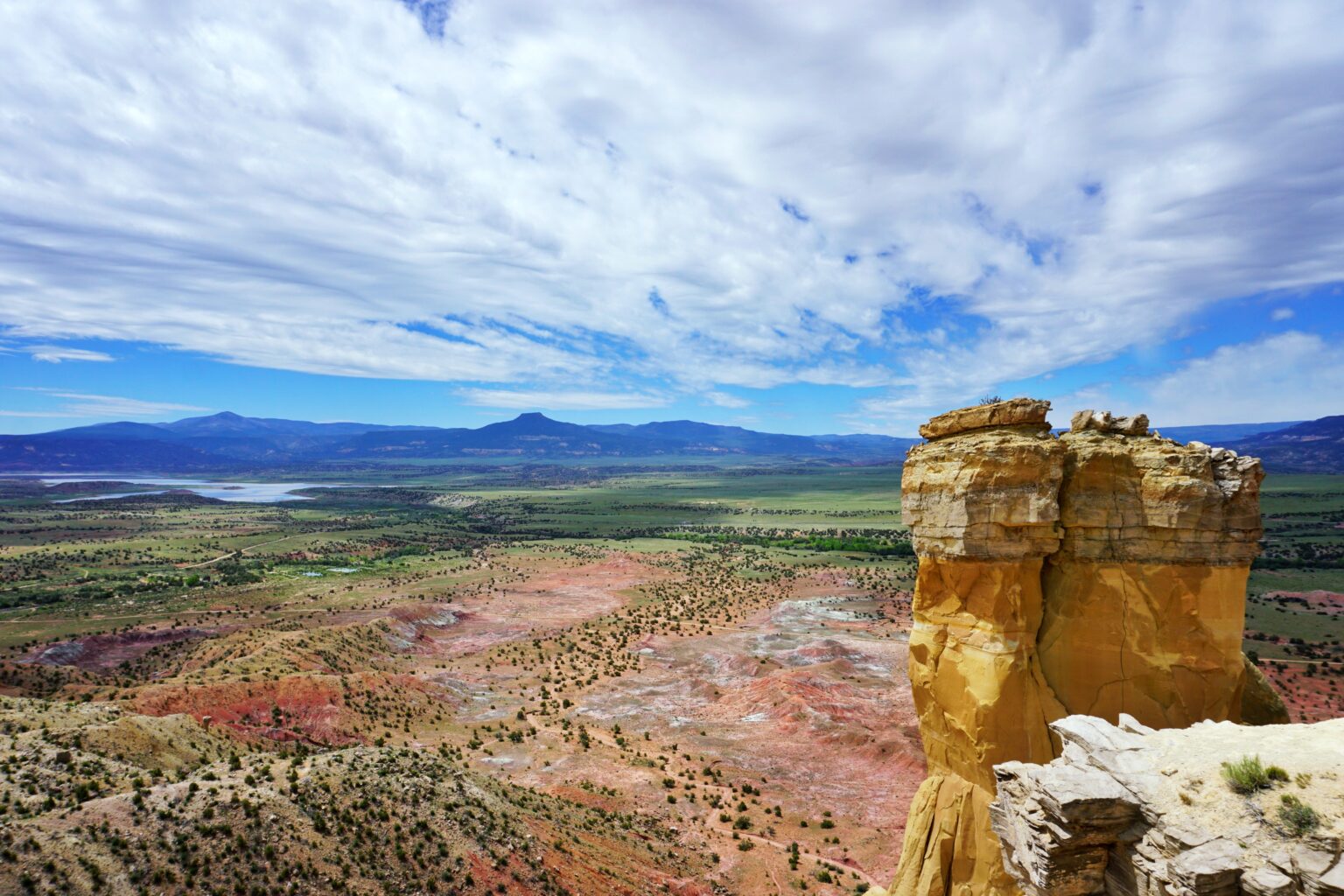 A breathtaking landscape in Abiquiu, New Mexico, featuring a mix of volcanic ash formations, red rock cliffs, and vast expanses of piñon-juniper forests.