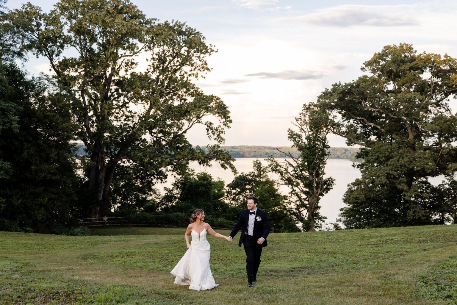 Bride and groom walking hand-in-hand along the serene Potomac River at River Farm, basking in the warm glow of a sunset amidst lush gardens and natural beauty, creating a romantic and unforgettable moment.