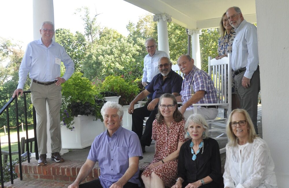 Ten people face the camera, standing or sitting on a brick porch.