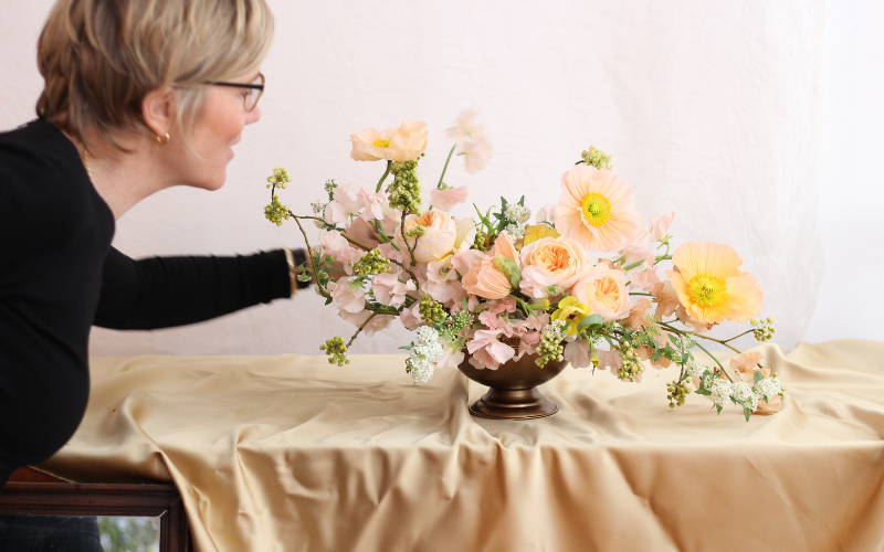 A person in a black top adjusts a colorful flower arrangement in a vase.