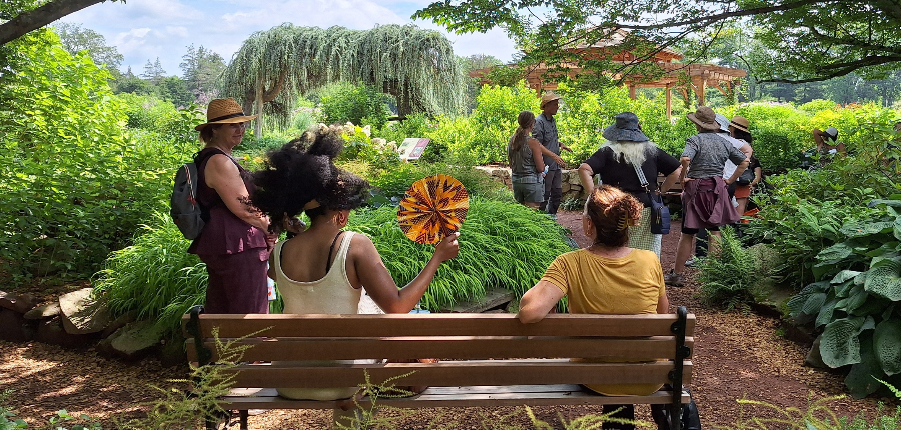 Two people sit on a bench in a lush outdoor garden.