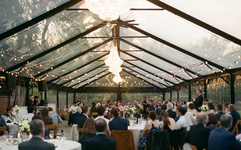 Guests at a wedding at River Farm under a clear-topped event tent in a garden.