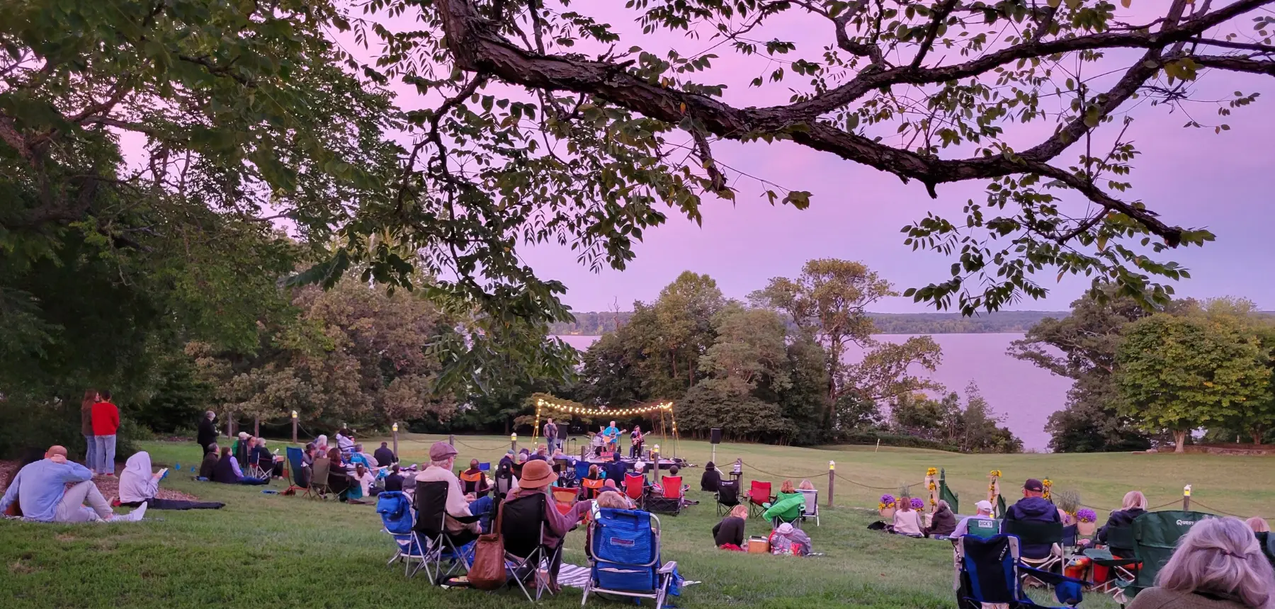 People sitting on the lawn at a River Farm Music at the Manor concert at sunset